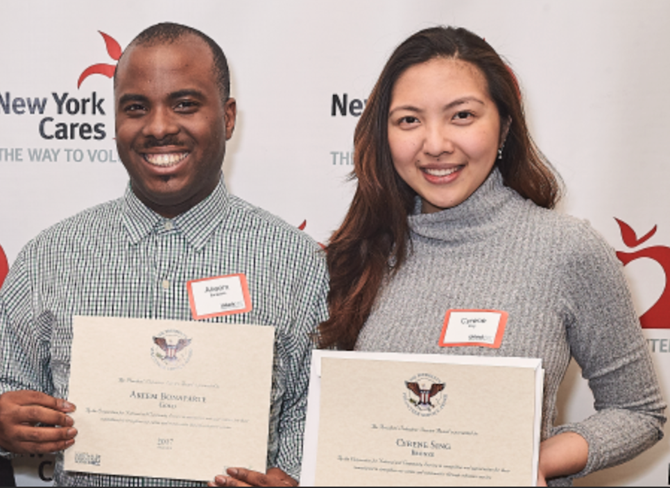 Two individuals hold certificates in their hands and smile at the camera